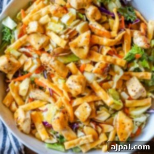 chopped chicken salad in a white bowl on a table with chicken, wonton strips, soy ginger dressing
