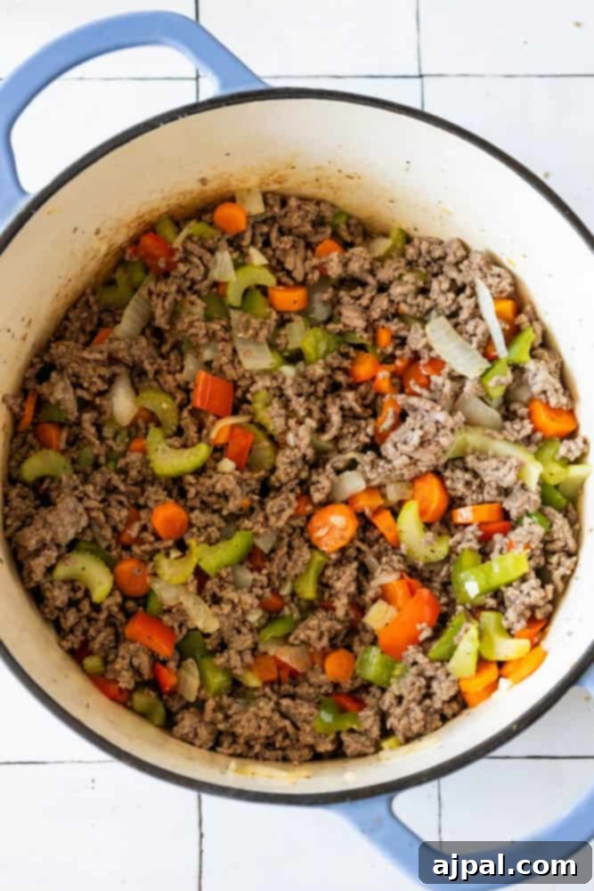 Easy One Pot Cheeseburger Soup Recipe with ground beef and vegetables cooked in a blue pot.