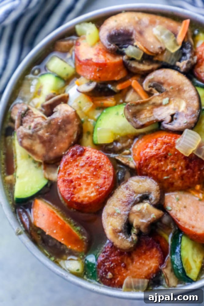 A delicious sausage and vegetable soup recipe with mushrooms, zucchini, and andouille sausage, simmering in a pot.