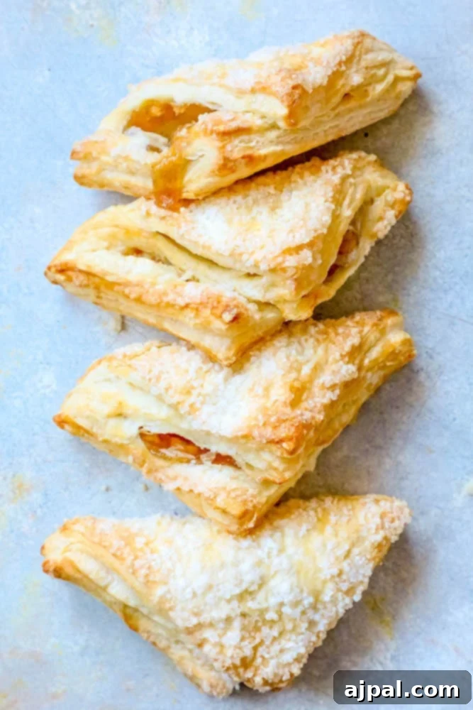 A delightful stack of fluffy puff pastry apple turnovers with a generous dusting of powdered sugar, set against a calming blue background, promising a sweet indulgence.