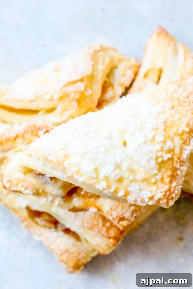 A tempting stack of homemade apple turnovers, lightly dusted with powdered sugar, showcasing their flaky crust and golden perfection, ready to be served.
