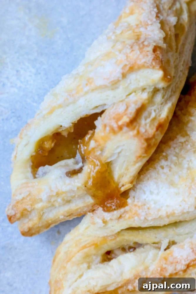 Two exquisite apple turnovers with a hint of apricot filling visible, presented beautifully on a white plate, ready for a delightful indulgence.
