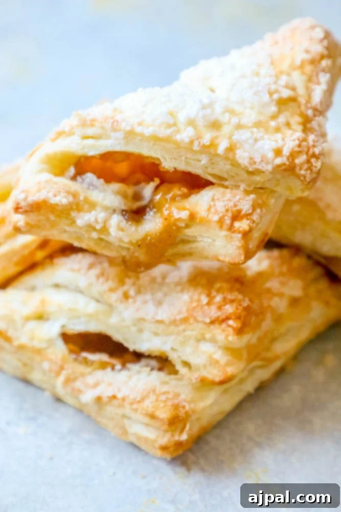 A close-up of several bakery-style apple turnovers, showing their flaky golden crust and enticing texture, perfect for any time of day.