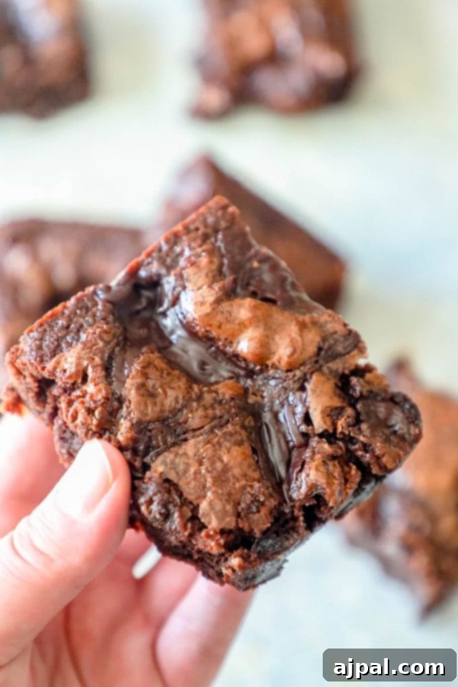 A hand gently holds a single, perfectly cut fudgy brownie, showcasing its rich texture and decadent appearance.