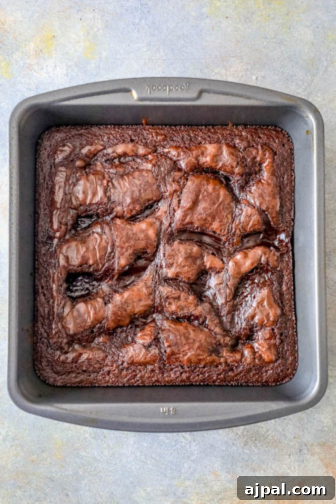 A pan filled with freshly baked, fudgy brownies, with hot fudge drizzled generously over the top, ready to be cooled and cut.