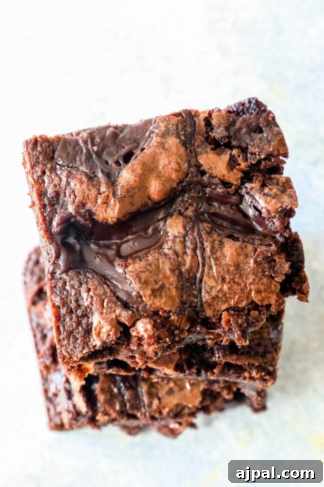 A stack of four rich, fudgy brownies topped with a generous drizzle of hot fudge sauce, showcasing their delectable layers and irresistible texture.