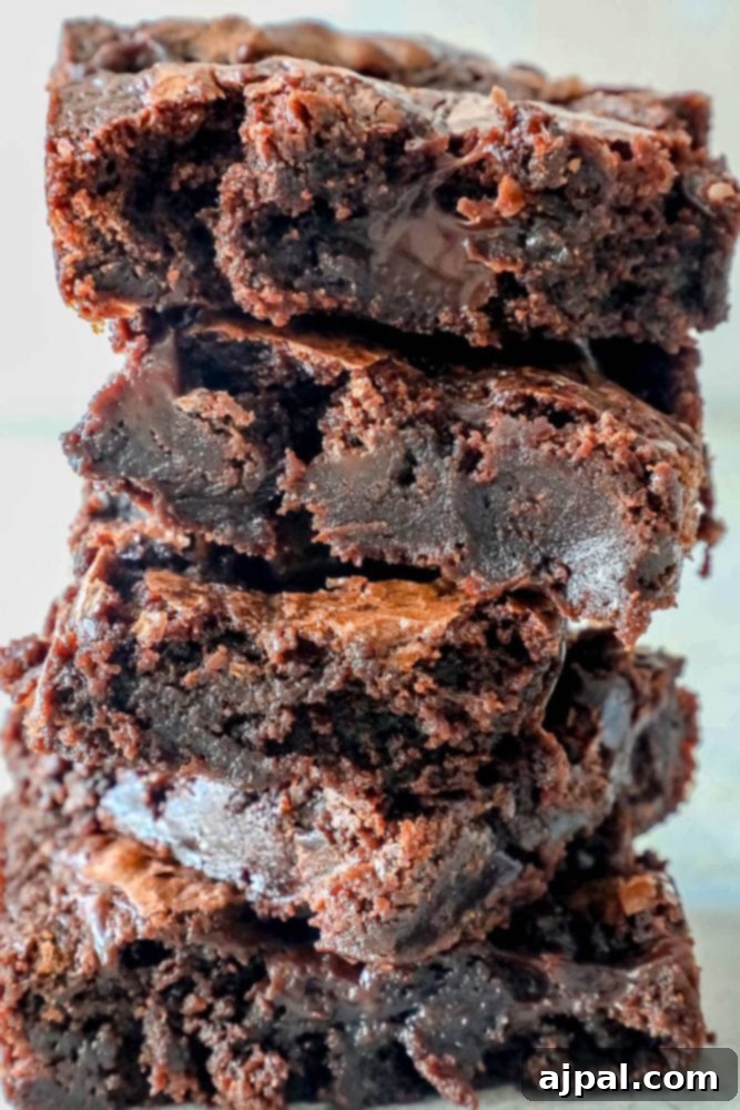 A stack of five perfectly cut fudgy brownies with a generous drizzle of hot fudge sauce, beautifully presented on a clean white plate.