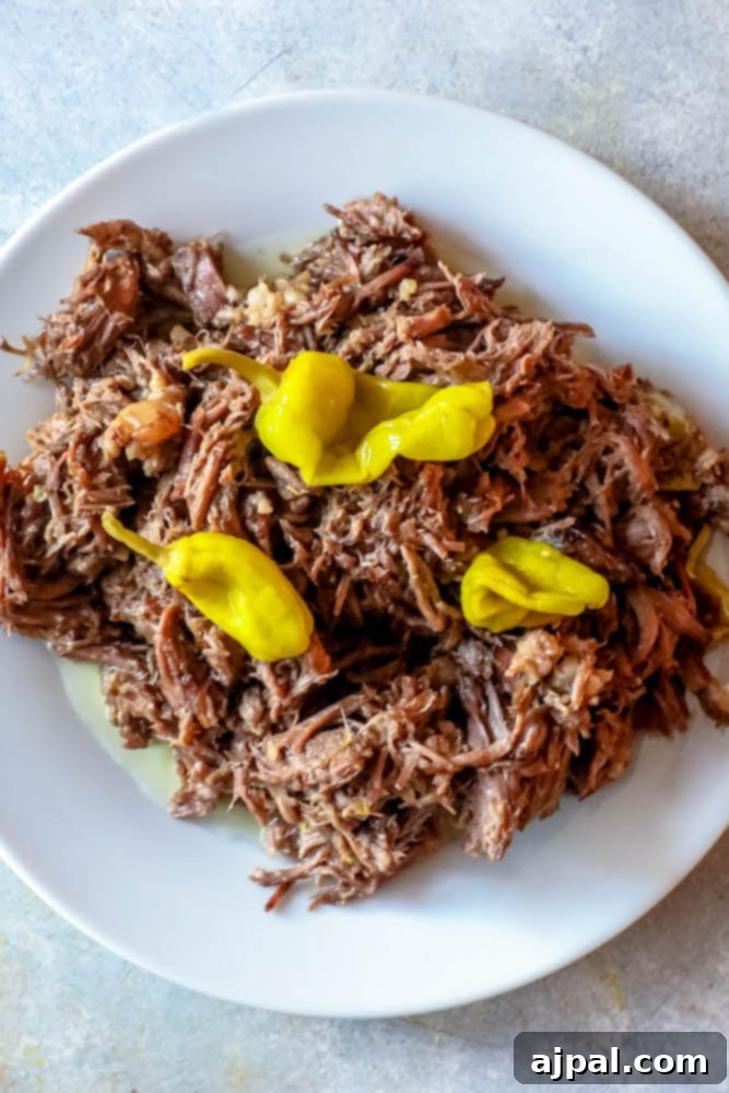 Southern Slow Cooker Pot Roast 2 Shredded Mississippi Roast with vibrant pepperoncini peppers served on a pristine white plate, showcasing its tender texture.