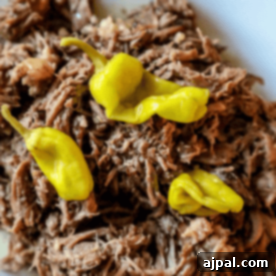 A plate of shredded meat from an Easy Mississippi Roast topped with three yellow chili peppers.