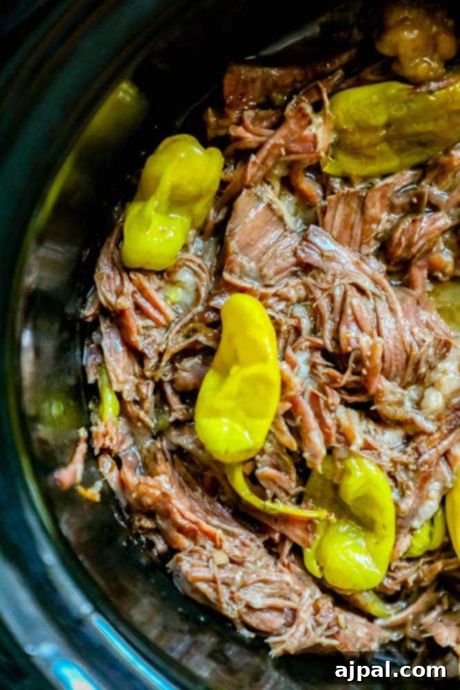 A slow cooker filled with tender beef and bright yellow pepperoncini peppers, ready to be shredded for Mississippi Pot Roast.