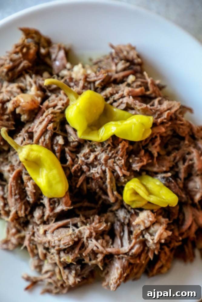 Close-up of shredded pot roast with bright yellow pepperoncini peppers on top, showcasing the dish's irresistible texture.