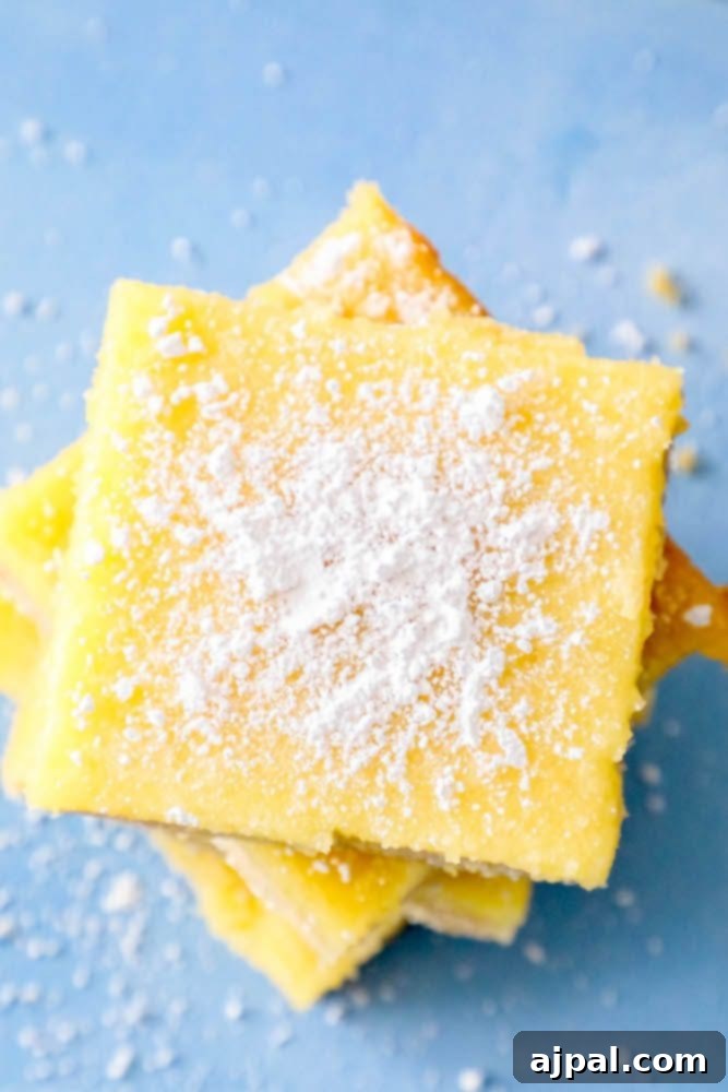 Picture of lemon bars stacked on top of each other with powdered sugar sprinkled on top, showcasing a golden crust and creamy lemon filling.