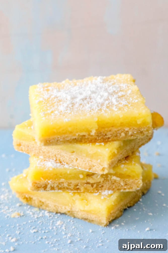 Picture of several lemon bars on a serving tray, glistening with powdered sugar.