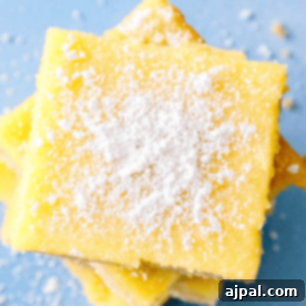 Close-up of the best lemon dessert bars stacked on a blue surface, delicately dusted with powdered sugar.