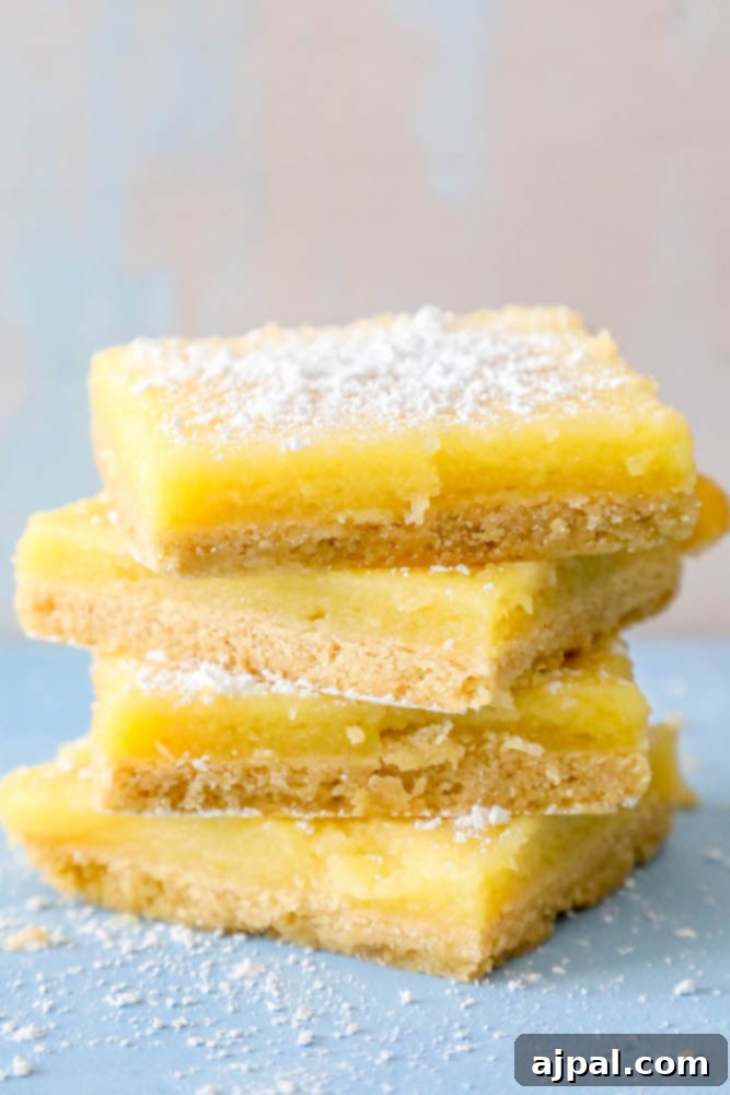 Picture of four golden lemon bars stacked neatly, dusted with powdered sugar, ready to be enjoyed.