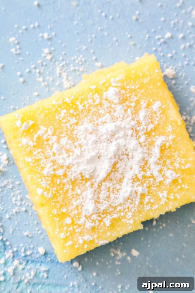 Close-up picture of a single lemon bar with a generous dusting of powdered sugar, highlighting its vibrant yellow and inviting texture.