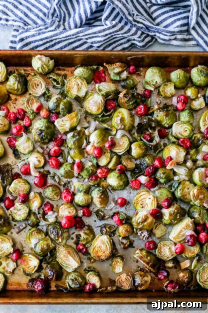 Close-up of perfectly baked Brussels sprouts with vibrant cranberries glistening on a sheet pan, ready to be served.