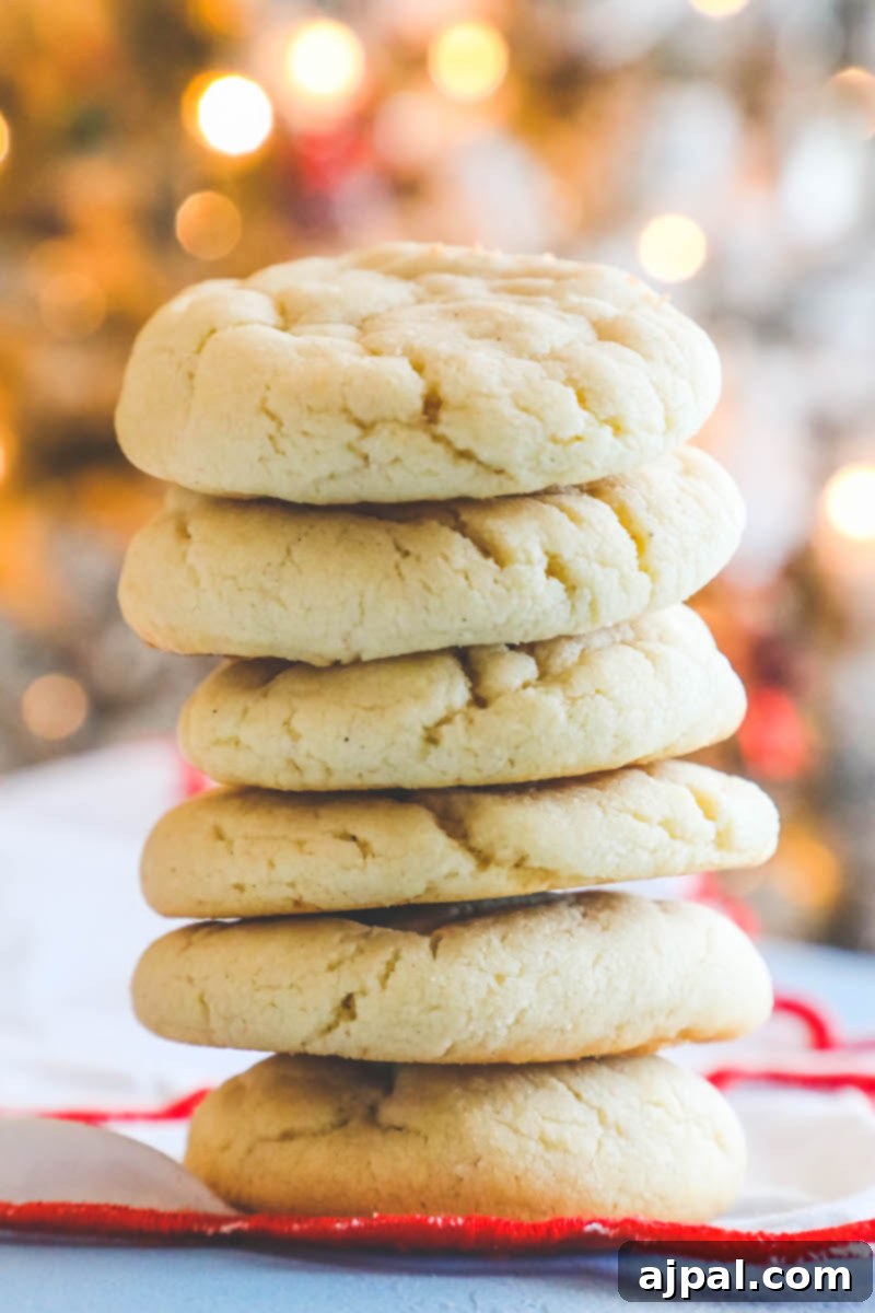 Seriously The Best Easy Chewy Sugar Cookies 4 A stack of the best sugar cookies, fluffy and perfectly golden, with a festive Christmas tree subtly blurred in the background, hinting at holiday cheer.