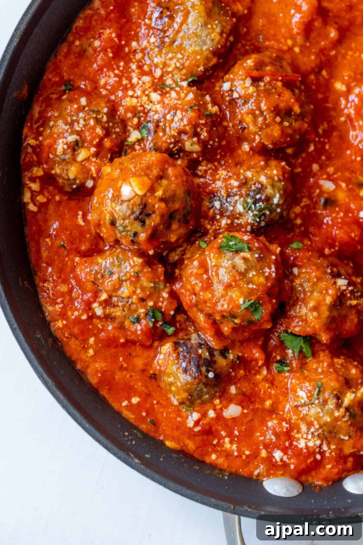 Perfectly Simple Meatballs 7 A frying pan filled with keto meatballs covered in a rich tomato sauce, garnished with chopped herbs and a sprinkling of cheese.