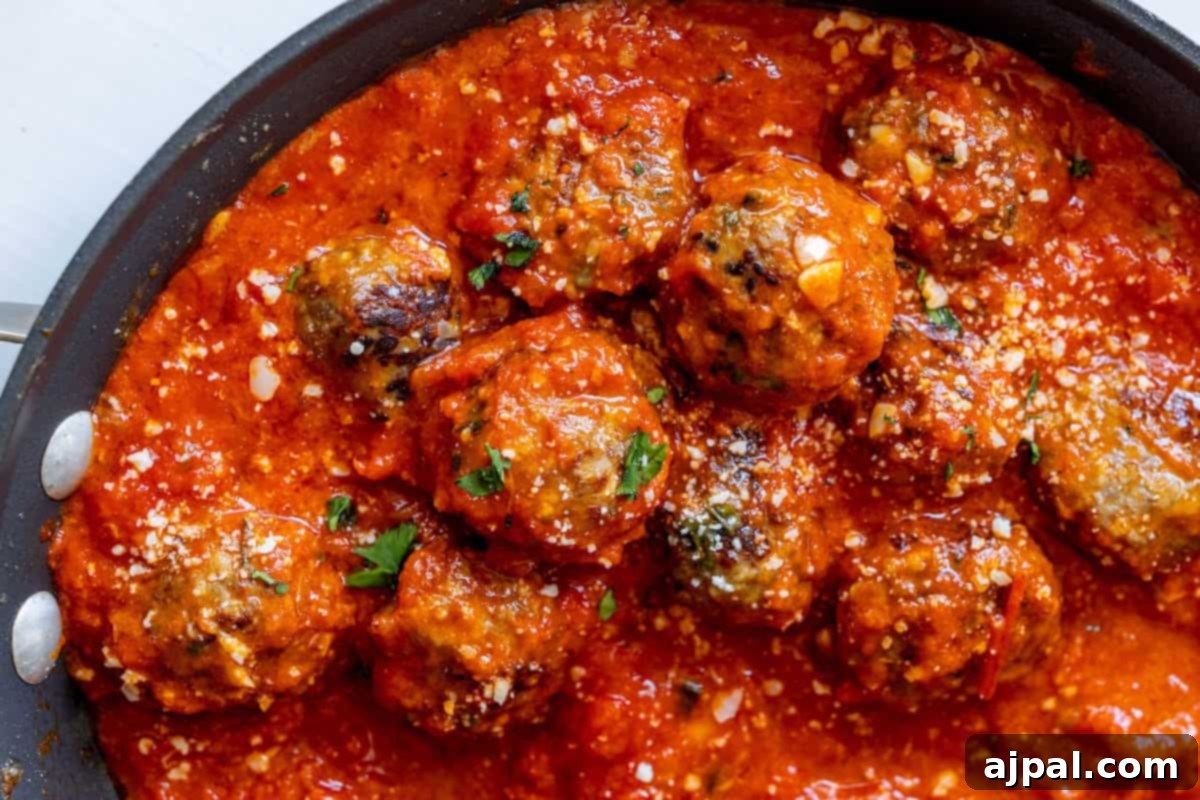 Perfectly Simple Meatballs 8 Close-up of a pan filled with meatballs in red tomato sauce, garnished with chopped herbs and grated cheese, showcasing an easy slow cooker meatballs recipe.