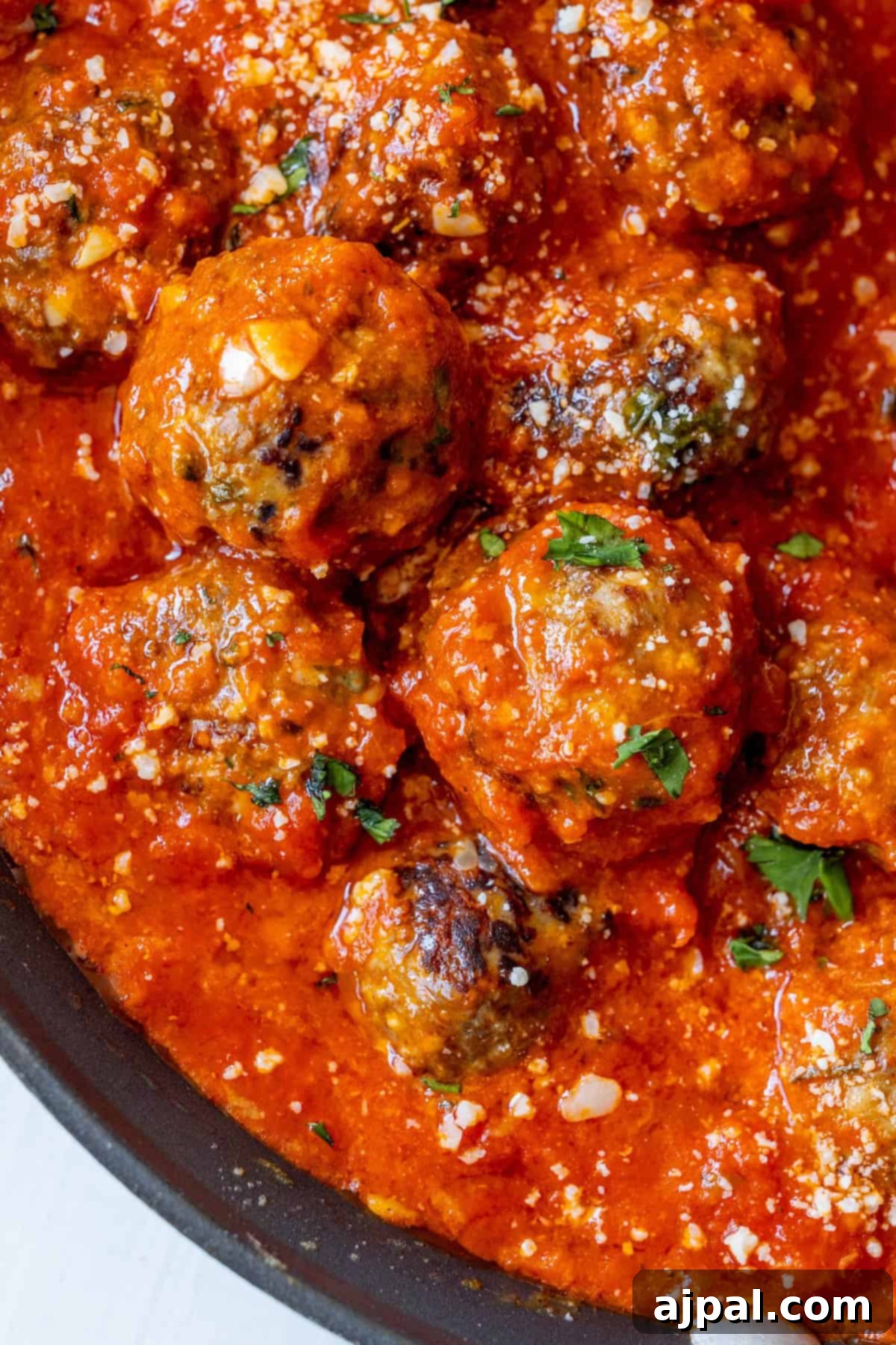 Deliciously Easy Meatballs 4 A close-up view of the best easy meatballs in a rich tomato sauce, garnished with chopped parsley and grated cheese.