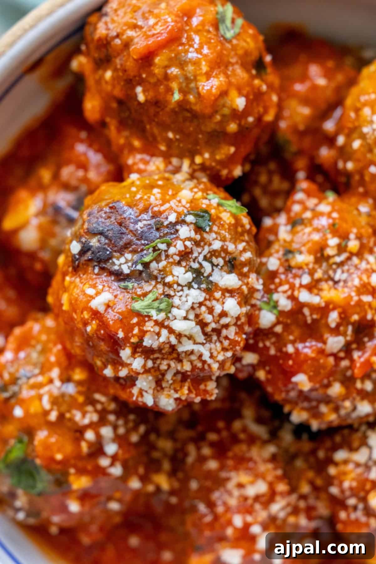 Deliciously Easy Meatballs 5 Close-up of the best easy meatballs topped with marinara sauce, grated cheese, and herbs.