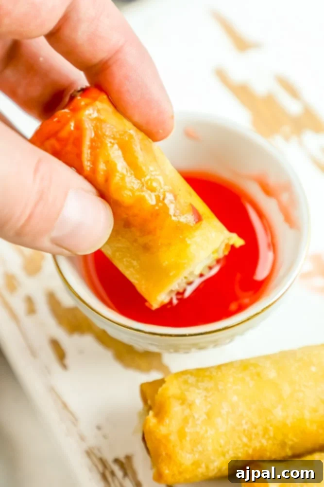 Crispy Homemade Egg Rolls 4 A person dipping a freshly made, crispy homemade egg roll into a rich red dipping sauce, highlighting its golden exterior.