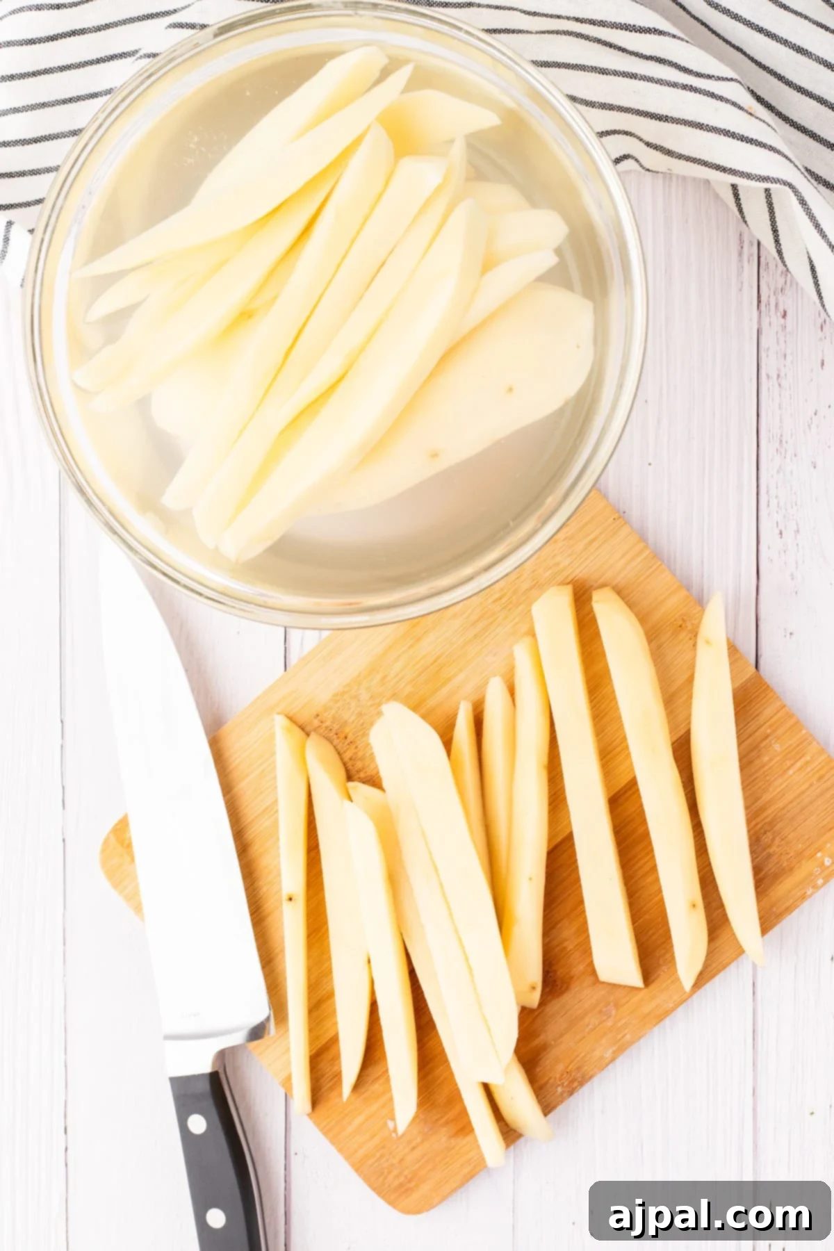 potato cut into fries on a cutting board next to fries soaking in water