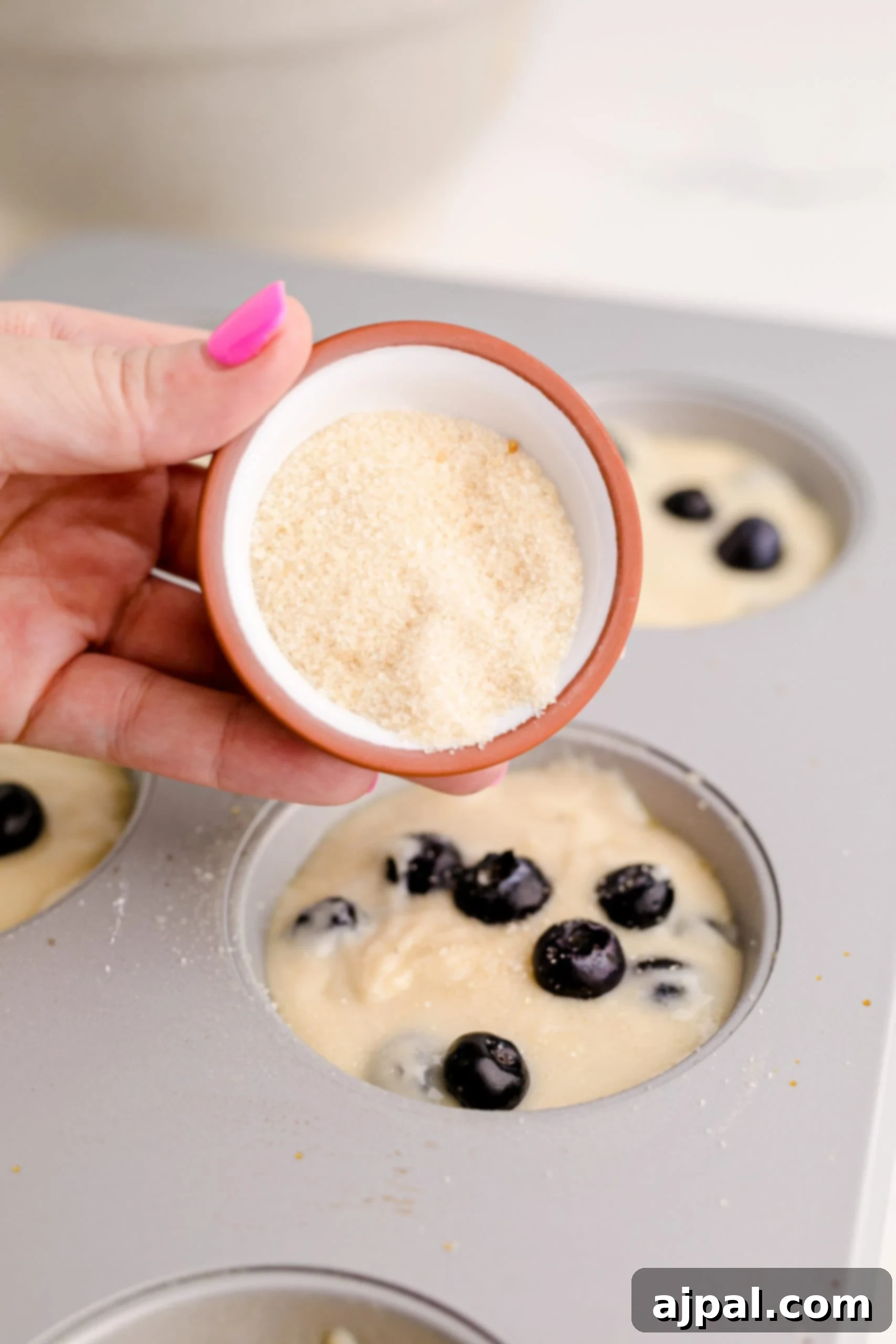 A person preparing jumbo blueberry muffins by pouring fresh blueberries into a muffin tin.