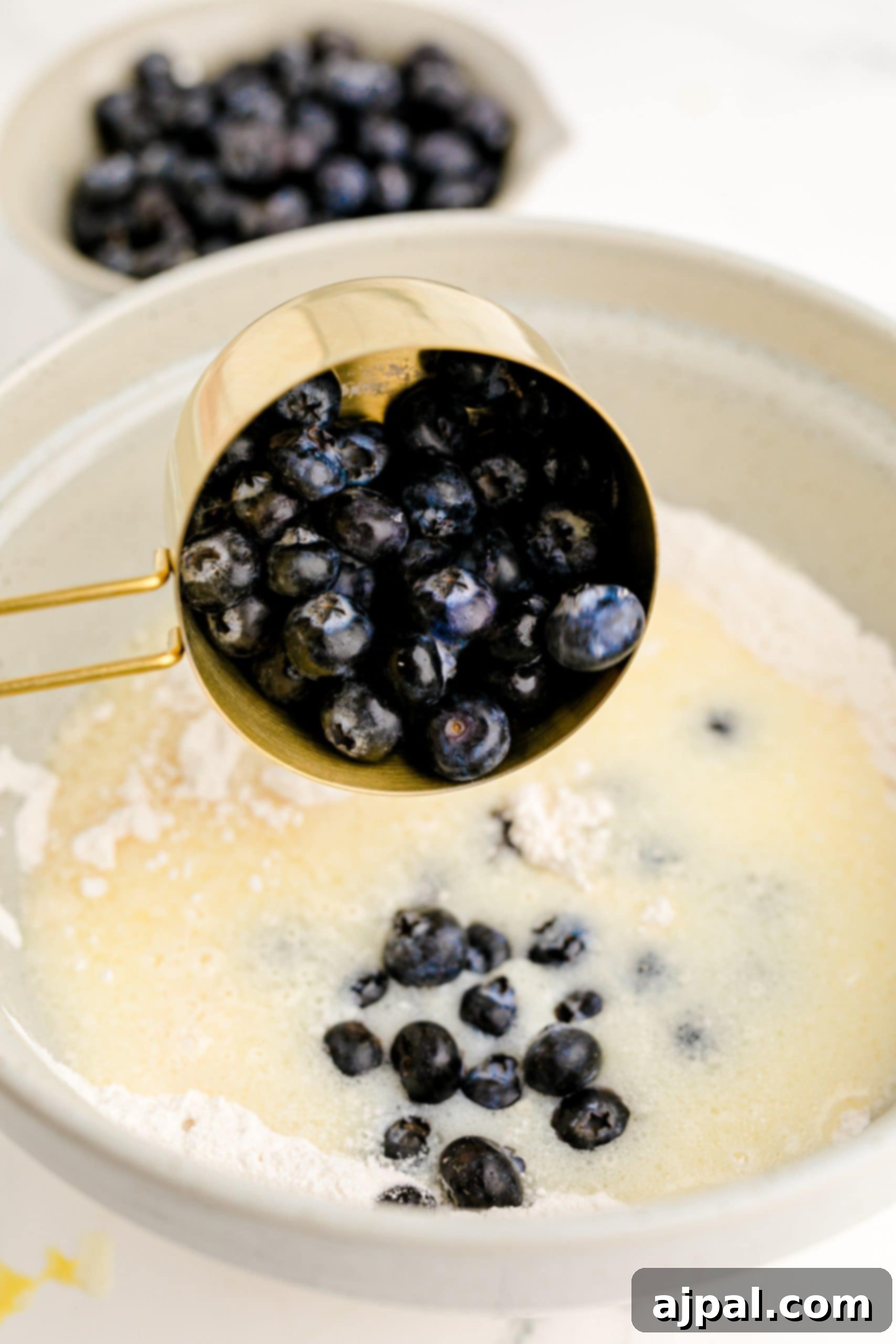 A blueberry recipe is being prepared by adding blueberries to a bowl of flour.