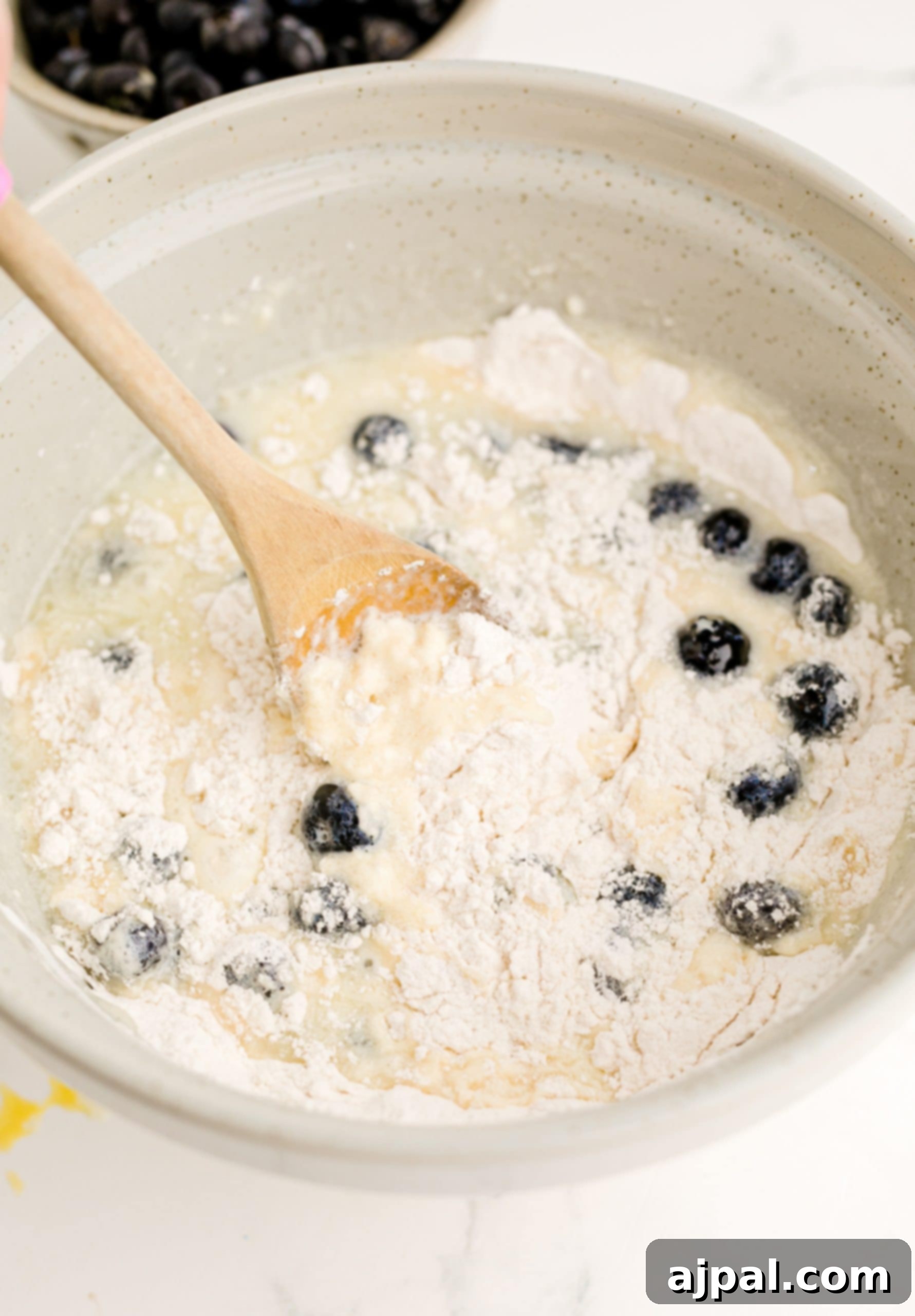 Blueberry pancake batter in a bowl with a wooden spoon.