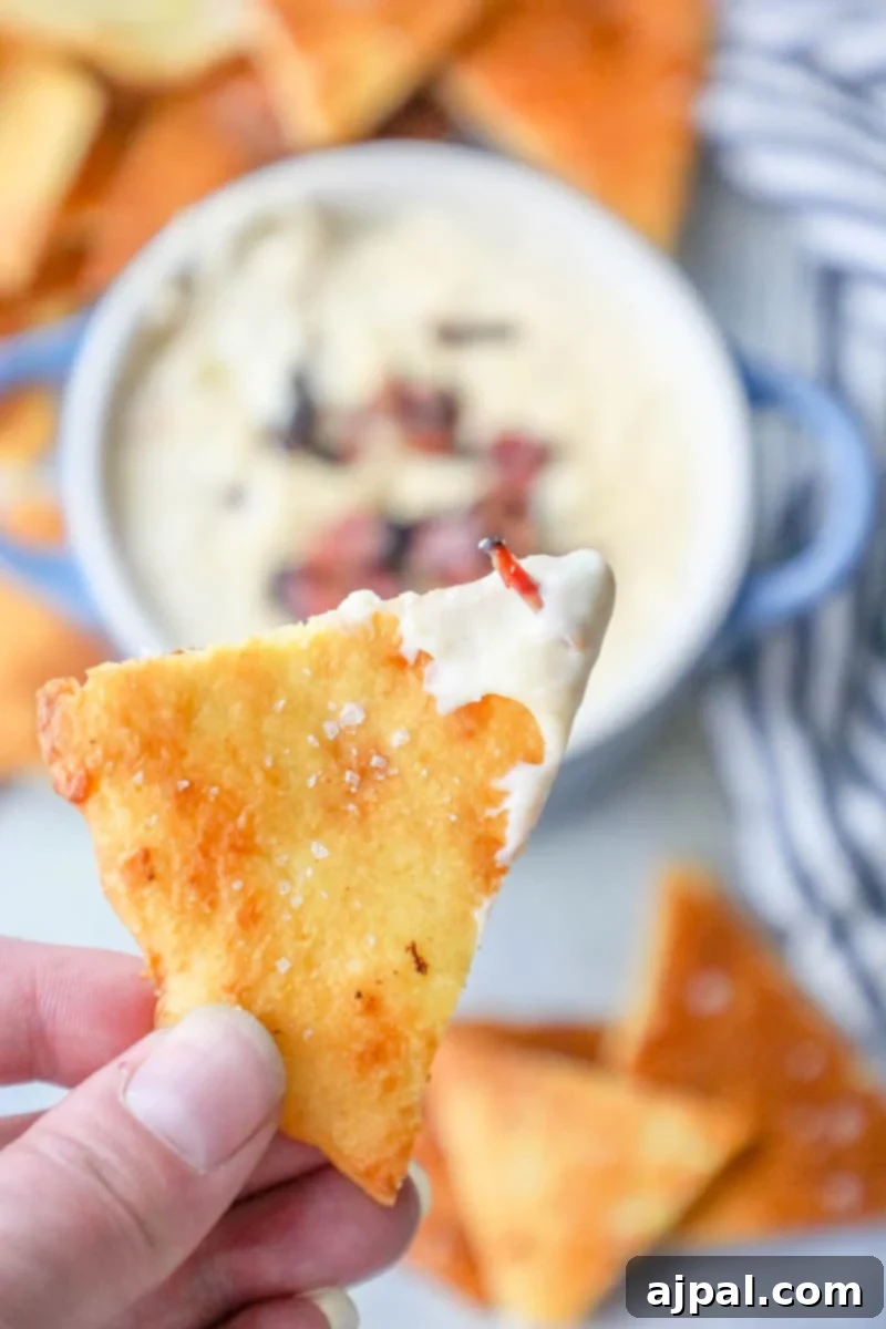 Quick Keto Tortilla Crisps 2 Picture of hand holding keto tortilla chip, topped with cheese and bacon, ready to be enjoyed.