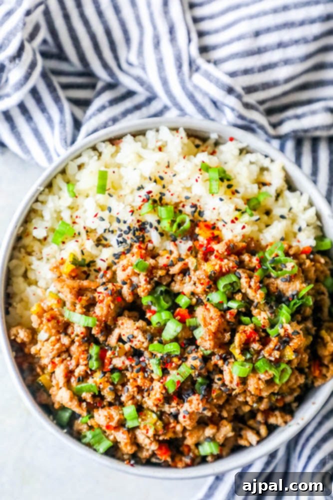 A top-down view of a delicious Keto Teriyaki Turkey Rice Bowl, garnished with sesame seeds and green onions, highlighting the appealing textures of the ground turkey and cauliflower rice.