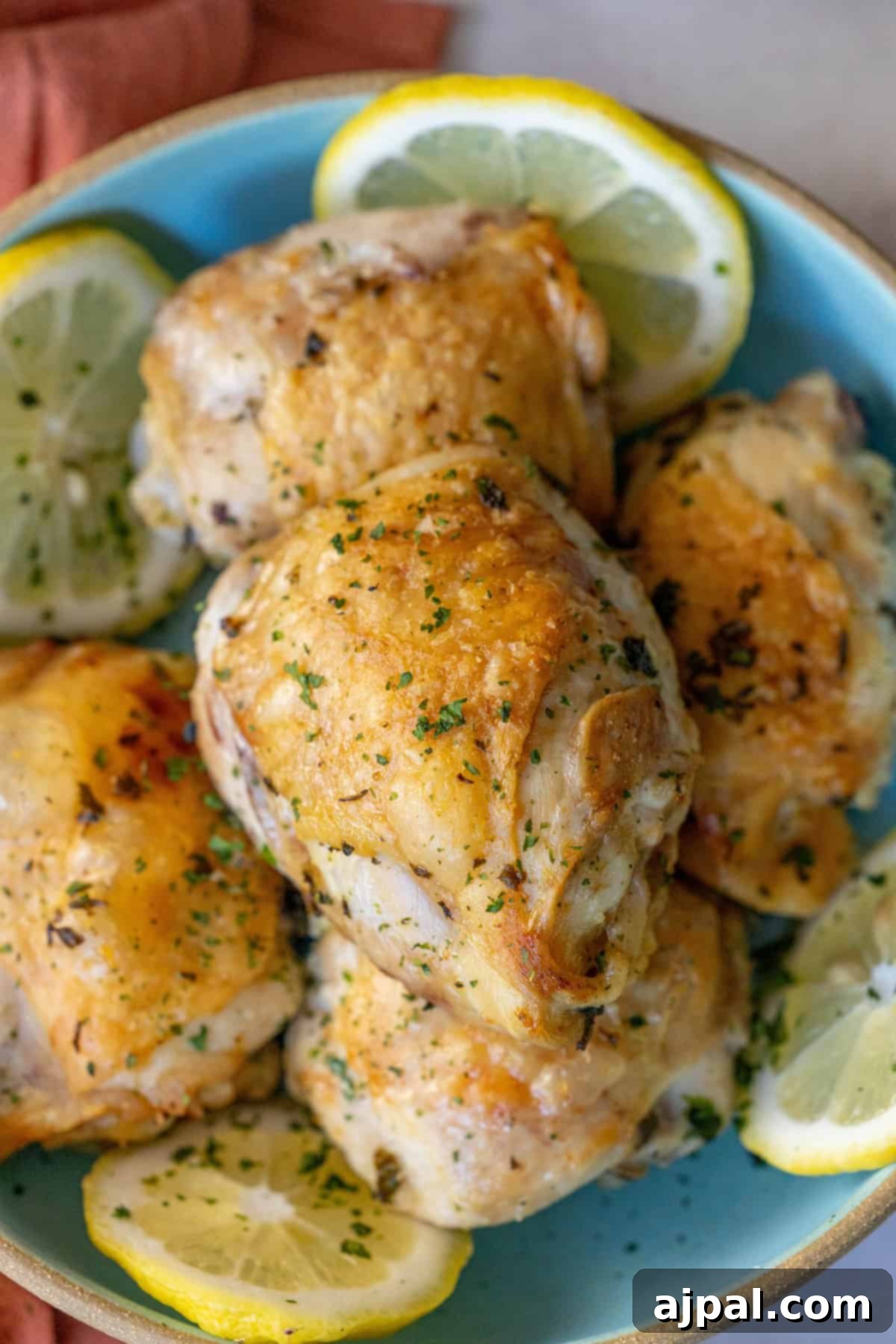 A blue plate showcases Easy Air Fried Lemon Chicken, with golden brown thighs garnished with chopped herbs and lemon slices.