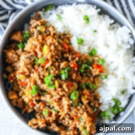 A bowl containing white rice and spicy Mongolian ground turkey garnished with green onions.