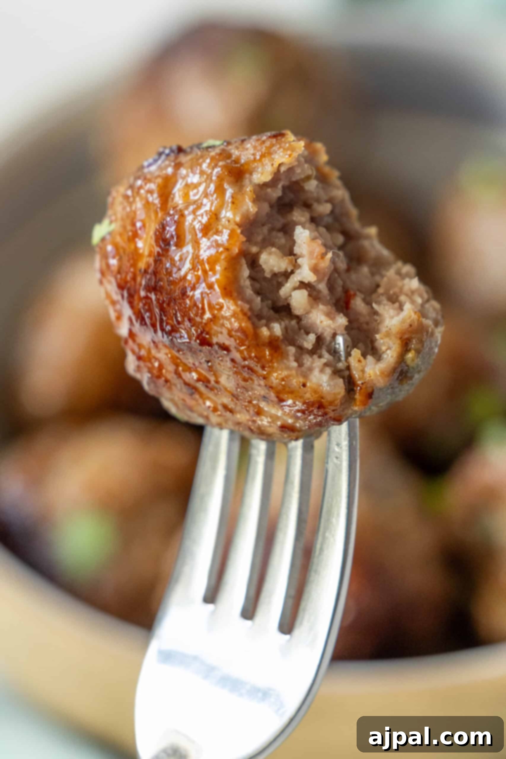 A fork holds a partially bitten air fried meatball, with more meatballs visible in the background.