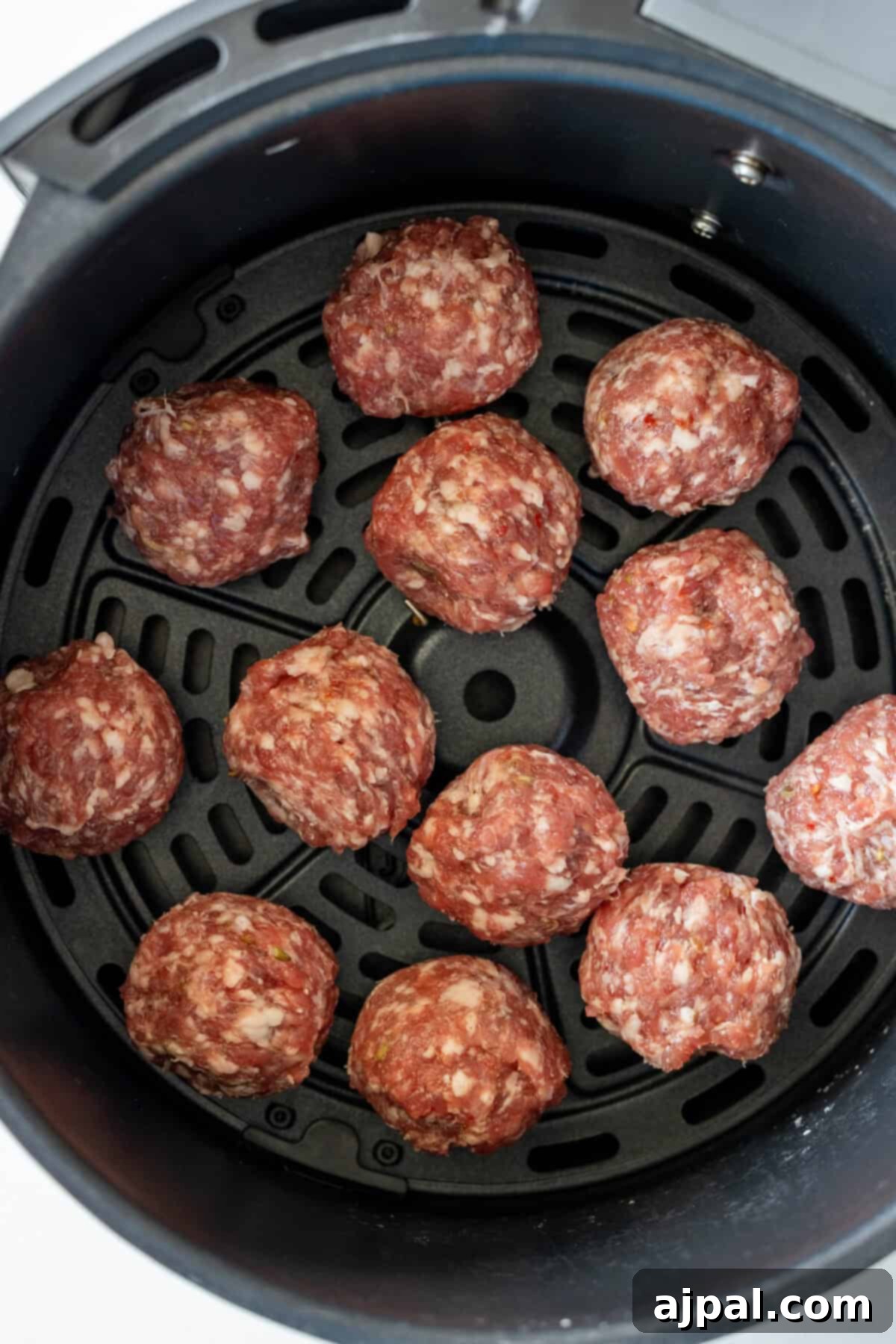 Raw keto meatballs recipe arranged in the basket of an air fryer.