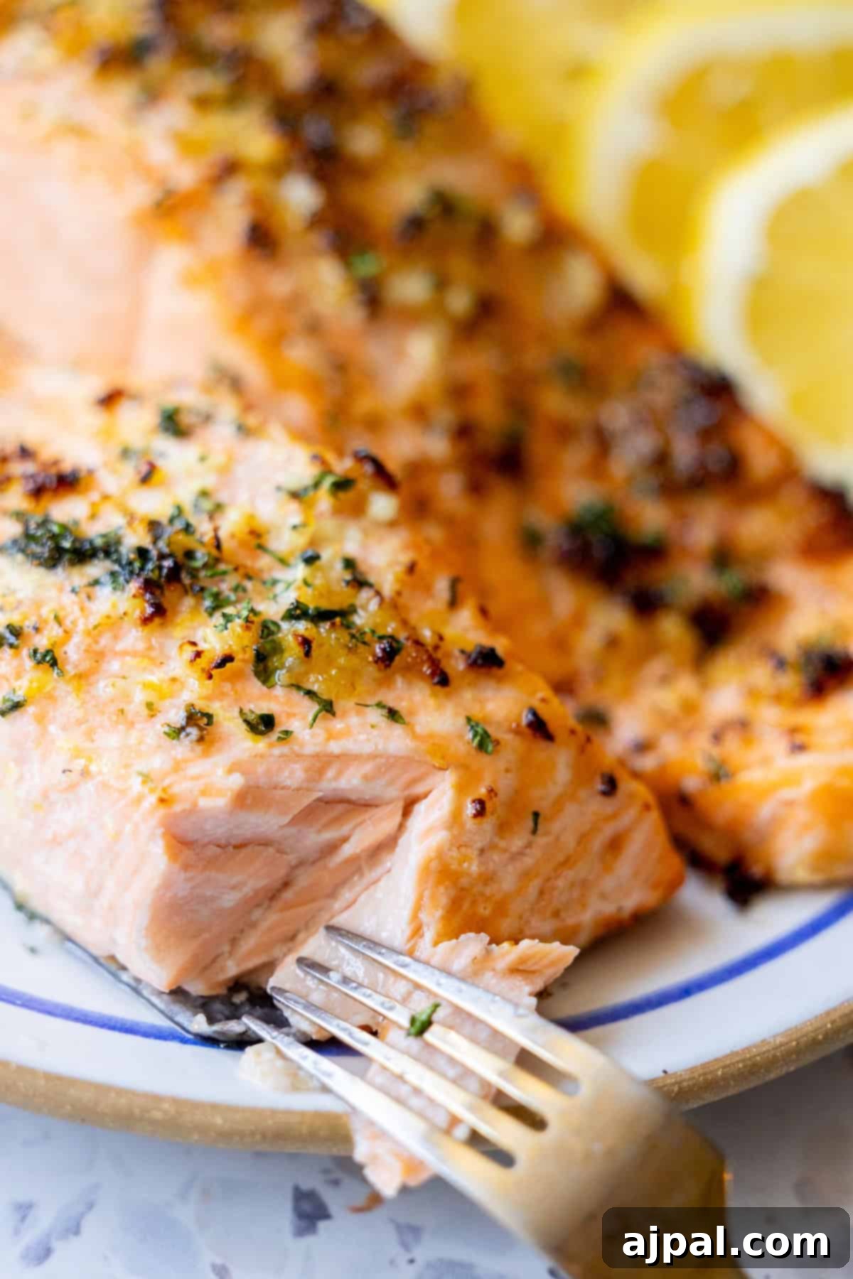 Easy Air Fryer Lemon Garlic Salmon 2 A fork flaking a piece of baked salmon topped with herbs, with lemon slices in the background on a plate—perfect for an Easy Air Fryer Lemon Garlic Salmon Recipe.