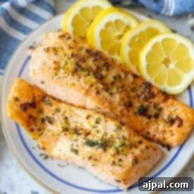 Two grilled salmon fillets garnished with herbs are served on a plate with three slices of fresh lemon, offering a delicious twist inspired by the Easy Air Fryer Lemon Garlic Salmon Recipe.