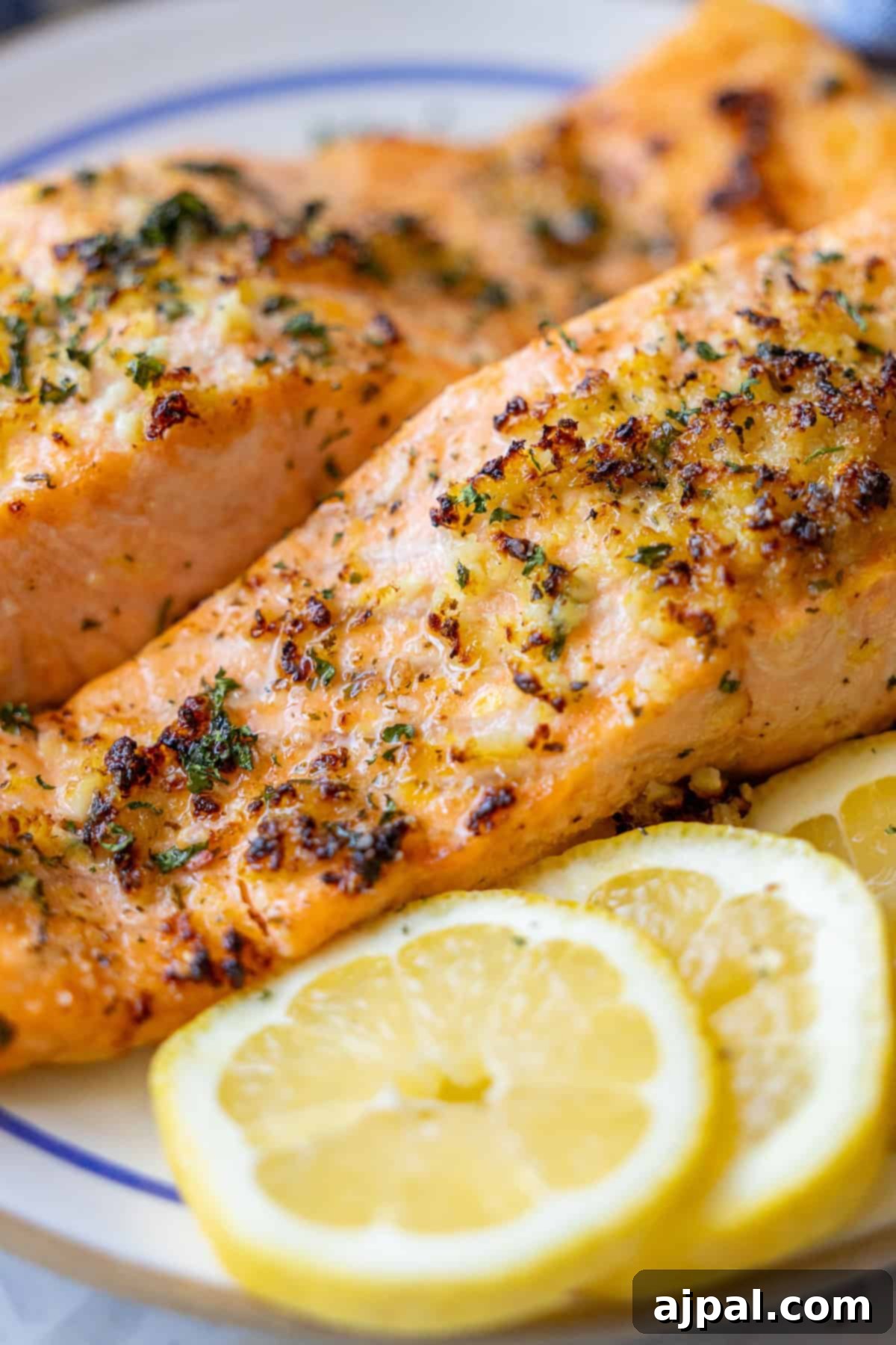 Easy Air Fryer Lemon Garlic Salmon 3 Two pieces of seasoned, baked salmon are served on a plate with three slices of fresh lemon in the foreground, capturing the essence of an Easy Air Fryer Lemon Garlic Salmon Recipe.