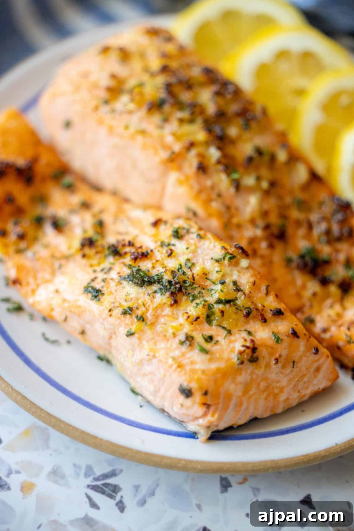 Easy Air Fryer Lemon Garlic Salmon 4 Two baked salmon fillets with herbs and seasoning on a plate, garnished with three lemon slices in the background—an easy air fryer salmon dish perfect for a quick keto air fryer salmon recipe.