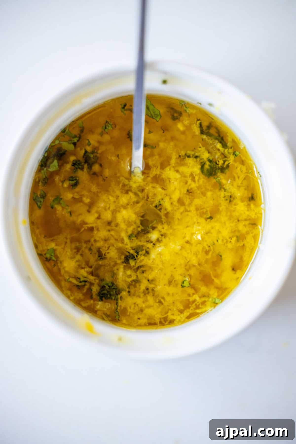 Easy Air Fryer Lemon Garlic Salmon 6 A close-up top view of a bowl containing a yellow mixture of oil, herbs, and grated zest with a spoon inside—perfect for making an Easy Air Fryer Lemon Garlic Salmon Recipe.