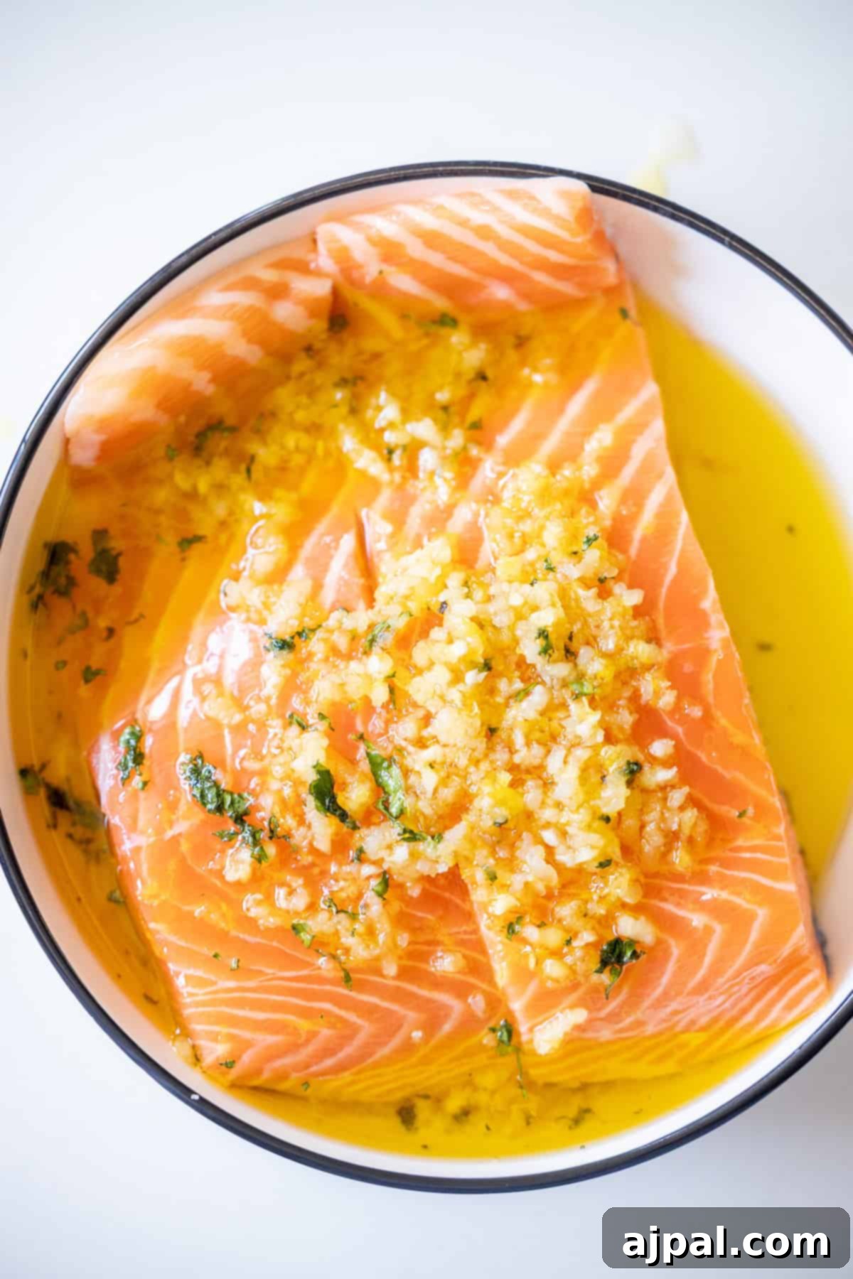 Easy Air Fryer Lemon Garlic Salmon 7 Raw salmon fillets marinating in a bowl with olive oil, minced garlic, herbs, and spices—perfect for an Easy Air Fryer Lemon Garlic Salmon Recipe.