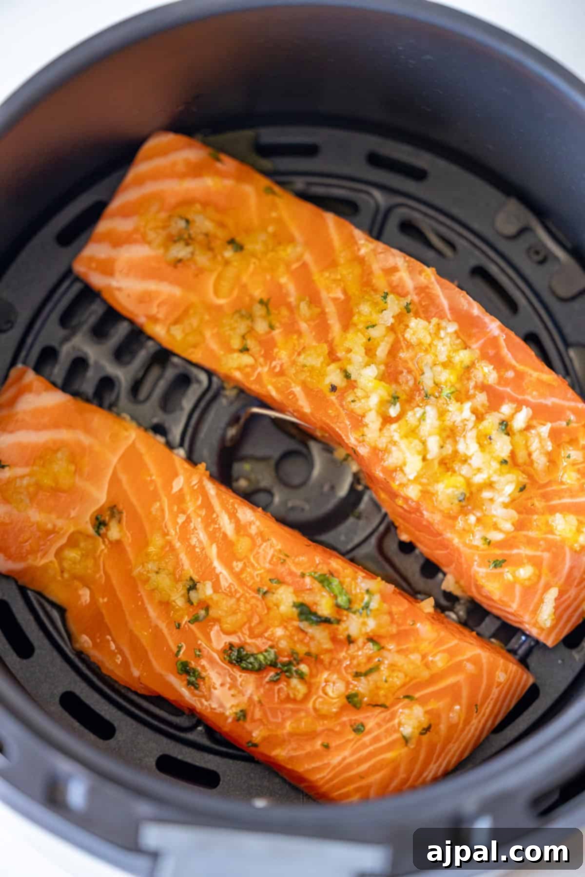 Easy Air Fryer Lemon Garlic Salmon 8 Two raw salmon fillets topped with chopped garlic and herbs placed inside an air fryer basket, ready to be cooked—an Easy Air Fryer Lemon Garlic Salmon Recipe perfect for learning how to air fry salmon effortlessly.