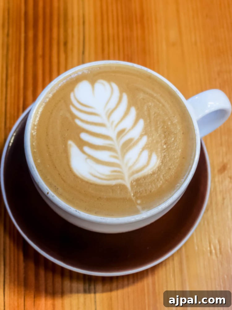 A latte with intricate leaf art sits on a rustic wooden table at a charming cafe in Atascadero.