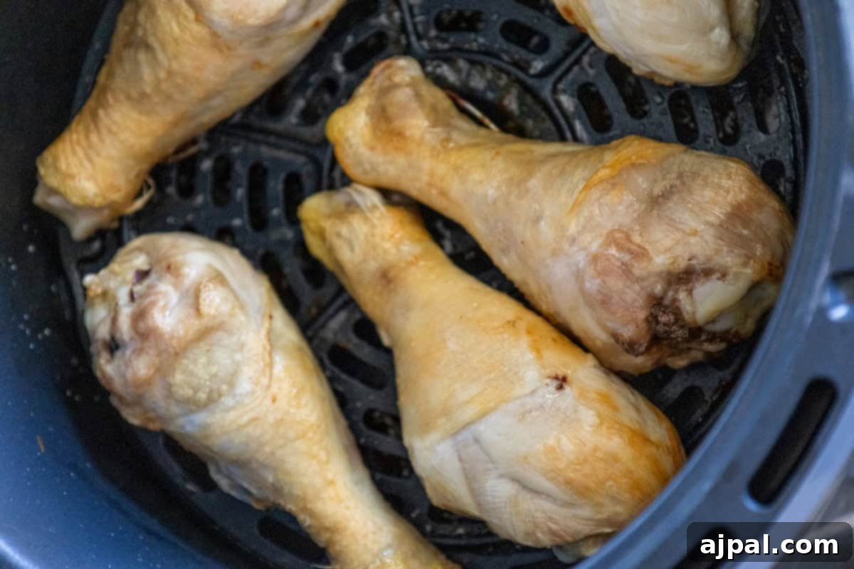 Four easy chicken drumsticks rest in an air fryer basket, perfectly poised for a crispy golden finish.