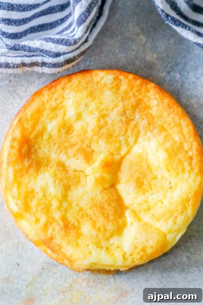 Close-up picture of a slice of golden-brown keto butter cake with a fluffy texture, resting on a white plate on a rustic wooden countertop with a towel.
