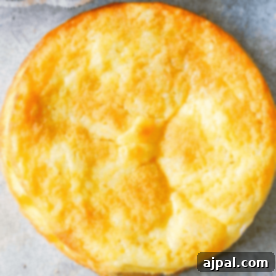 A small, perfectly baked golden-brown keto butter cake with a golden-brown crust, presented on a light gray surface, representing a delightful low-carb dessert.