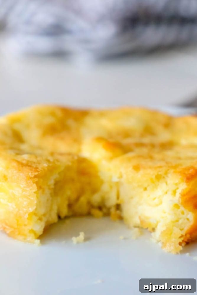 A close-up of a perfectly baked keto butter cake slice, with a single bite taken out, revealing its moist and tender interior, on a white plate.