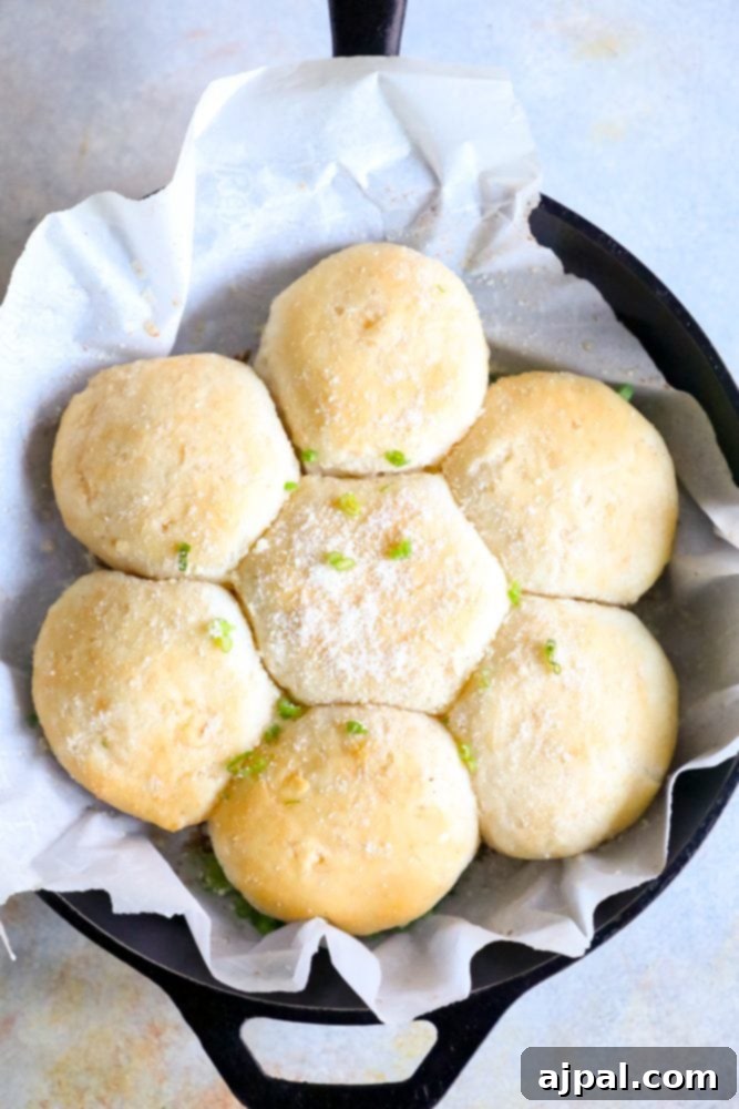 Seven golden brown garlic butter parmesan dinner rolls in a cast iron skillet, garnished with fresh green onions and grated parmesan cheese.